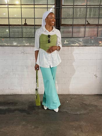 reviewer standing in a layered outfit with the corset in green over a button-up top and wide-leg trousers 