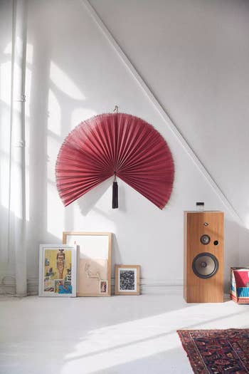 Room with a large fan decor on the wall, framed art pieces on the floor, and a wooden speaker. Stylish and modern home decor setup