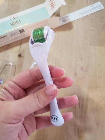 hand holding pink and green face derma roller