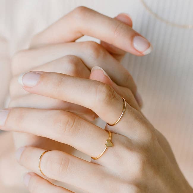 gold heart ring worn with other dainty bands on model's hand