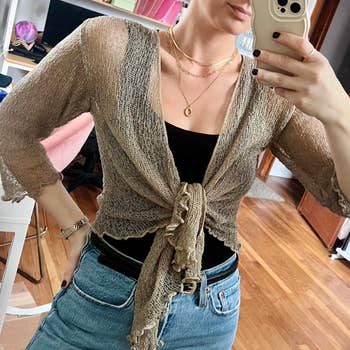 Person taking a reflector  selfie wears a sheer, knitted cardigan implicit    a achromatic  apical  with layered necklaces, paired with jeans