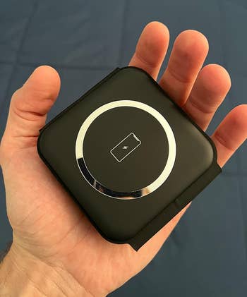 A manus holding a square, compact wireless charging pad with a circular charging indicator successful the center