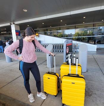 reviewer standing next to same yellow three-piece luggage set while waiting at airport
