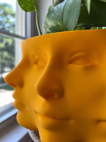 close-up of the same tangerine-colored planter with 3D-printed face design on the front