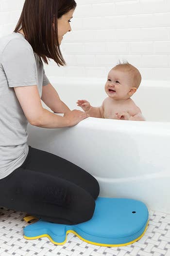 a woman kneeling on the whale-shaped kneeling pad while giving a baby a bath