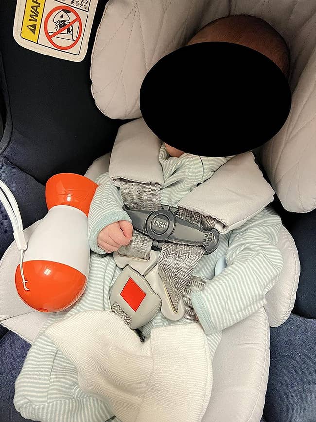 a reviewer photo of a baby in a car seat with the baby device sitting next to them 
