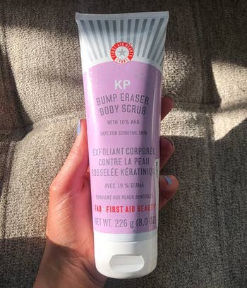 Hand holding FAB First Aid Beauty KP Bump Eraser Body Scrub conduit  with 10% AHA for delicate  skin
