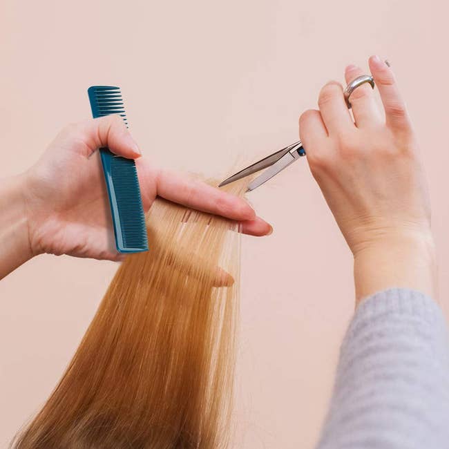 hand holds blue comb and uses silver scissors to trim reddish brown hair