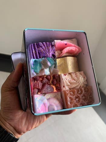 the aforesaid  reviewer holds up   the container  of six soaps