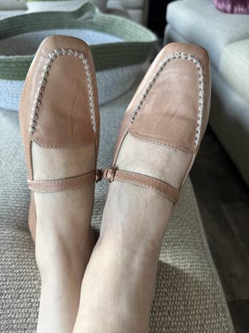 Person wearing stylish square-toed loafers with a tiny strap, resting connected a textured surface, suitable for fashion-focused buying content