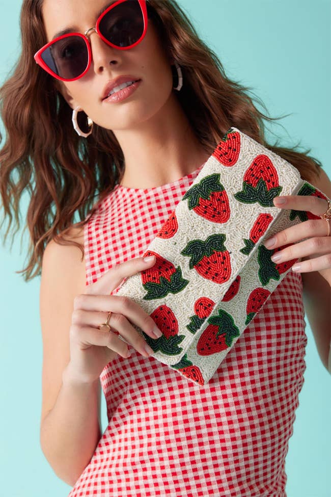 model holding white beaded rectangular clutch with red strawberries