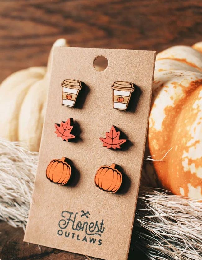 three pairs of stud earrings with one shaped like a to-go coffee cup, one shaped like a leaf, and the other shaped like pumpkins 