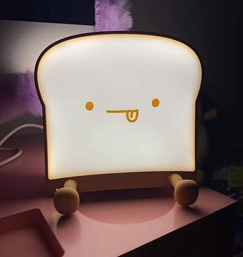 reviewer photo of the illuminated toast night light with its tongue sticking out in a dark bedroom