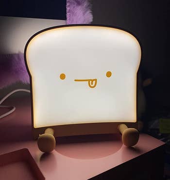 reviewer's illuminated toast night light with its tongue sticking out in a dark bedroom