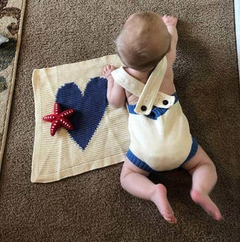 a baby crawling next to a cream colored baby blanket with a navy blue heart