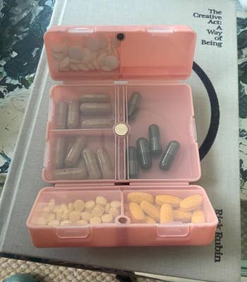 A pink folding organizer open to show capsules inside of the clear-paneled compartments 