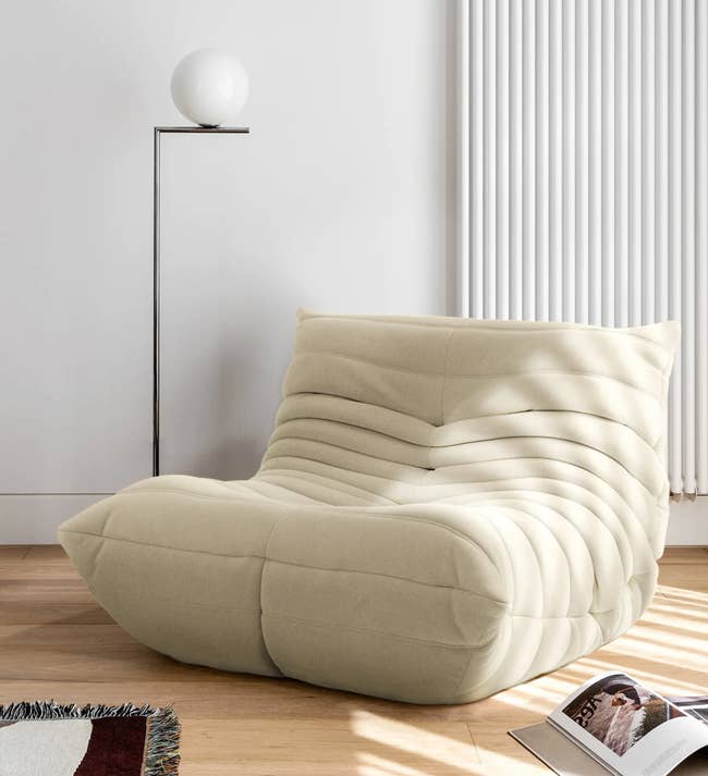 Cream curved bean bag lounge chair with horizontal pleats on a hardwood floor