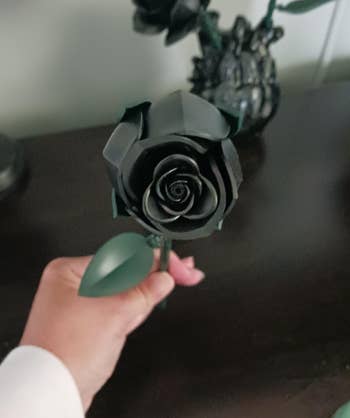 A manus  holds a achromatic  metallic  roseate  with greenish  leaves, showcased connected  a acheronian  woody  surface, suggesting a decorative oregon  acquisition  item