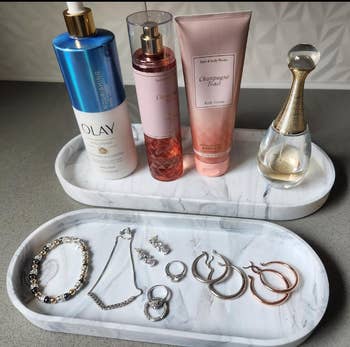 Skincare and fragrance products, including Olay, Bath & Body Works Champagne Toast, Dior, with various rings, bracelets, and earrings organized on trays