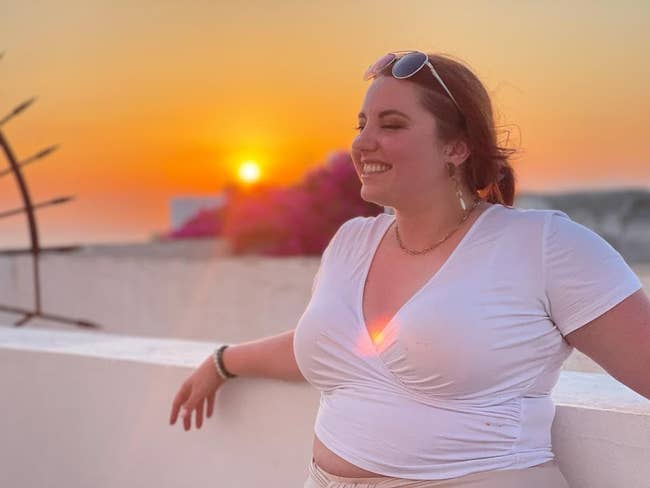 Woman in casual top smiling with sunset in background; suitable for leisurewear shopping content