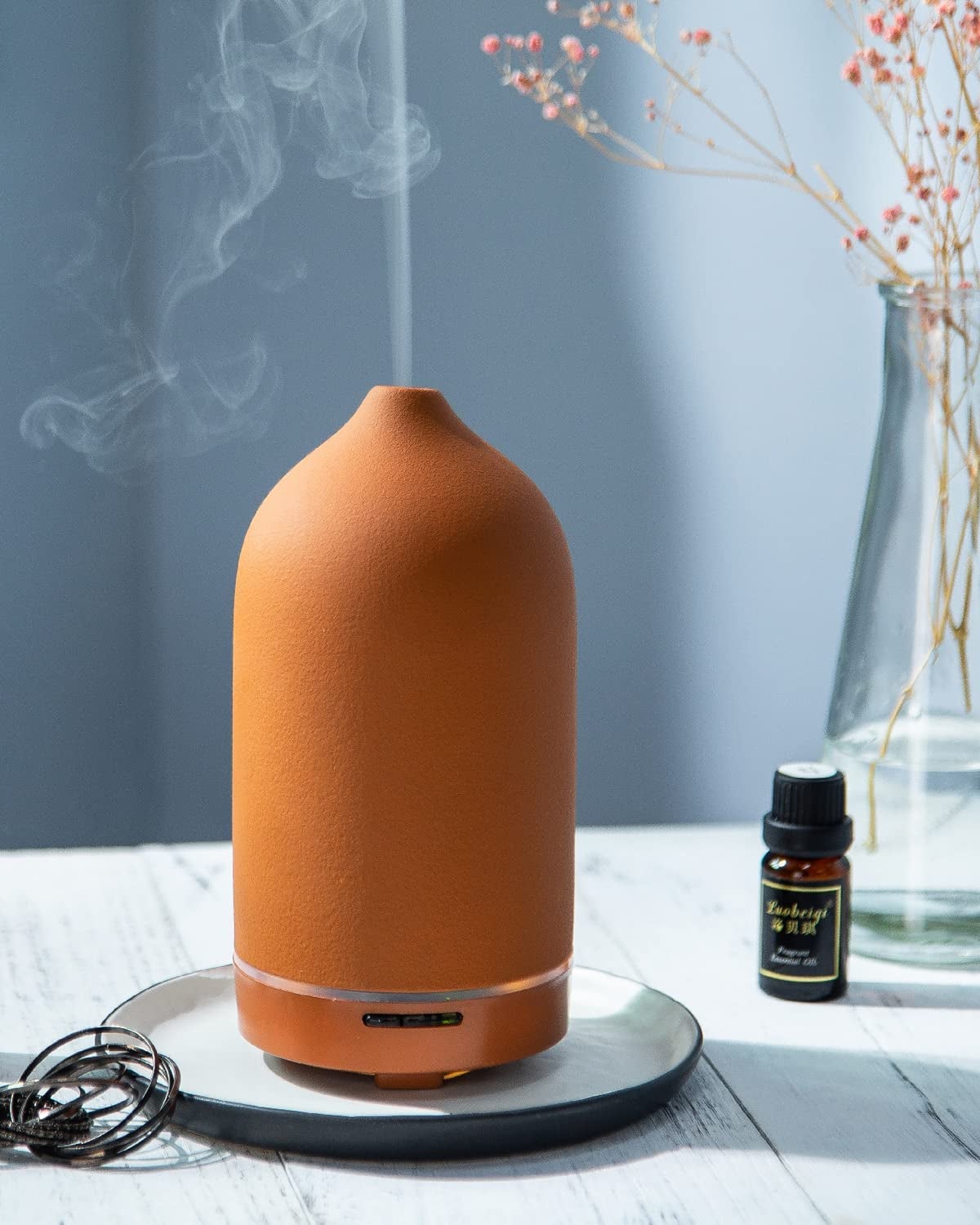a terracotta colored ceramic oil diffuser with mist coming out of the top