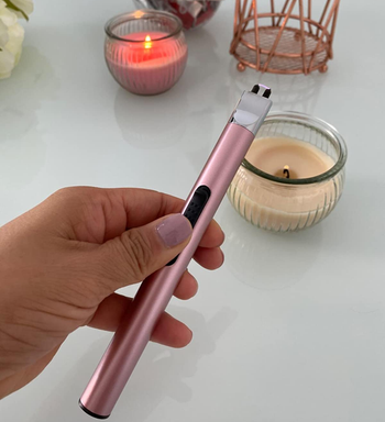 reviewer holding the pink electric lighter next to two lit candles