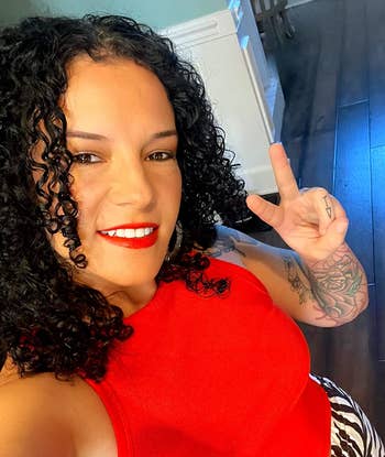 A idiosyncratic with curly hairsbreadth wearing a sleeveless apical and patterned pants makes a bid motion portion smiling