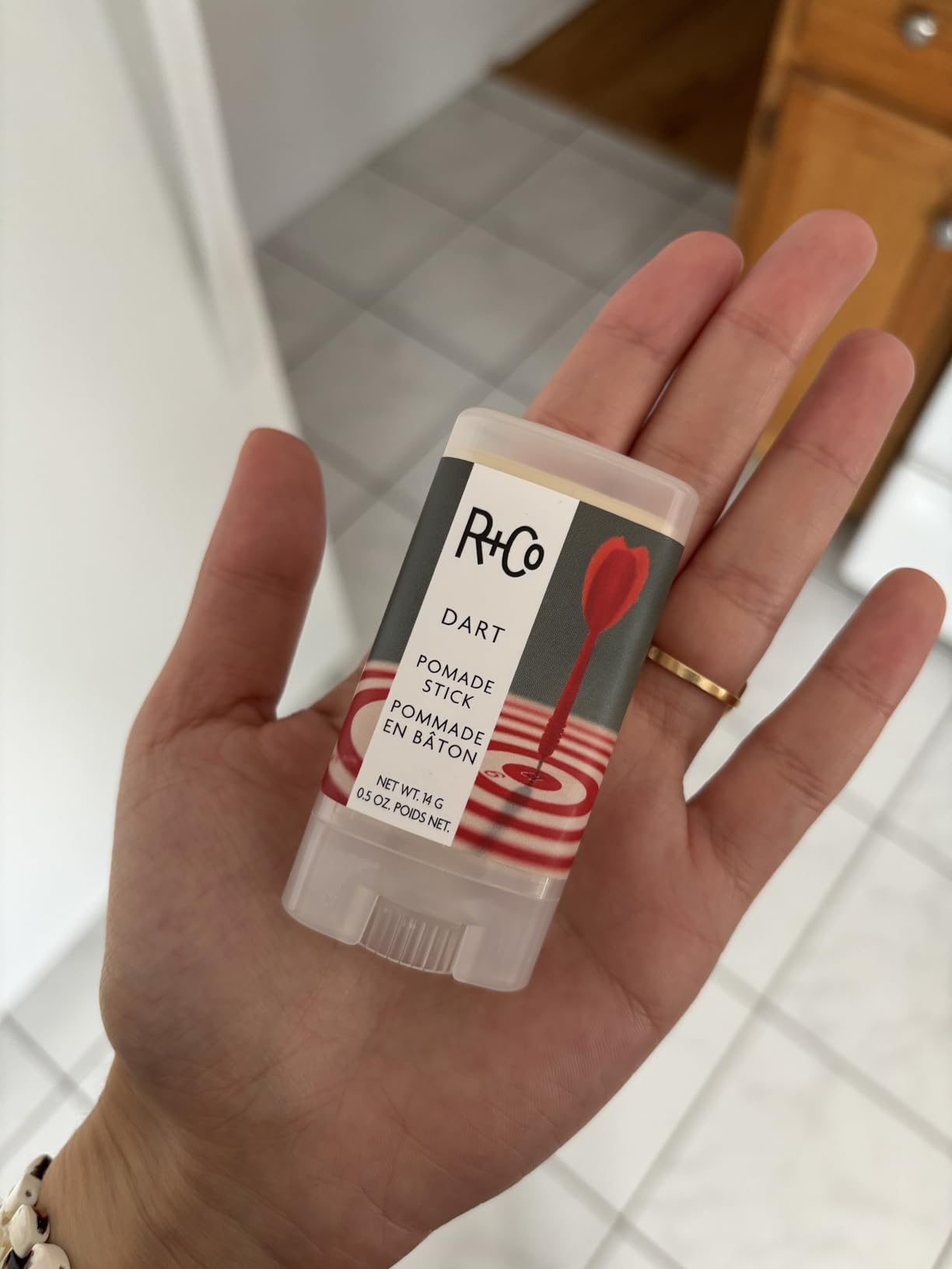 Hand holding R+Co Dart Pomade Stick with a modern design on the label, suitable for hairstyling