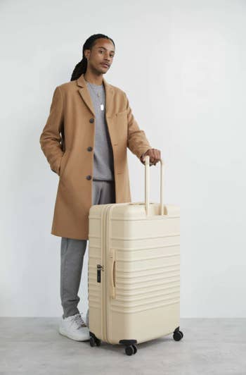 model standing next to white 29-inch large Béis suitcase with the handle up