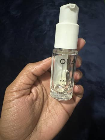 Hand holding a tiny vessel of Ouai hairsbreadth lipid with a pump dispenser