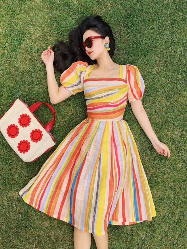 model lying on the ground wearing the linen midi dress, which has rainbow vertical stripes on it and slightly puffy sleeves