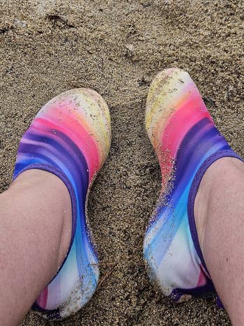 Feet wearing colorful, sand-covered water shoes on a sandy beach. Suitable for outdoor activities