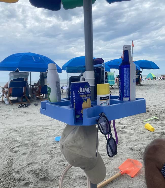 A blue silicone tray attachment wrapped around a beach umbrella rod holding up snacks and drinks 