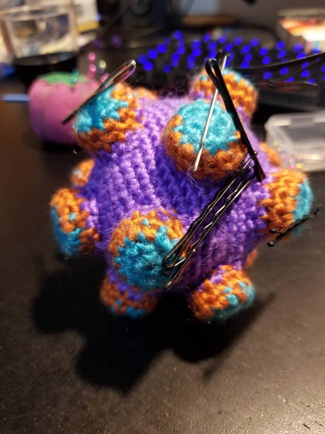 a crochet magnetic purple, blue, and orange katamari that's holding bobby pins