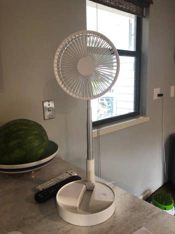 White fan standing on a circular base on a desk 