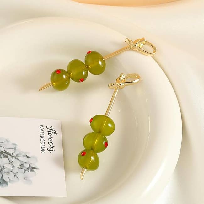 Gold toothpick shaped drop earrings with green bead accents resembling three olives on each