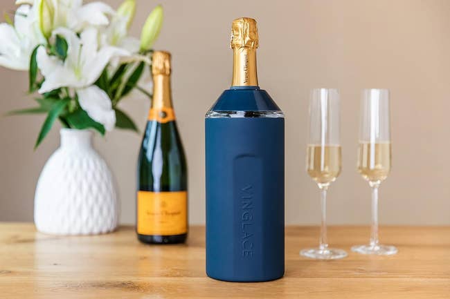 Champagne bottle in a stylish Vinglacé chiller with two glasses, set on a table next to a flower vase, emphasizing luxury and celebration