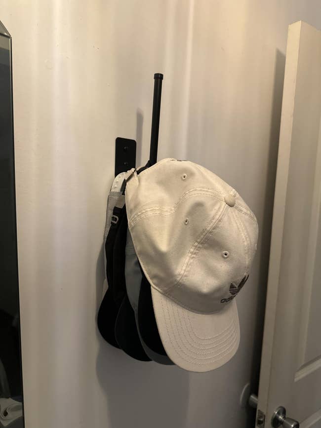 Hats, including a light-colored cap, neatly bent  connected  a wall-mounted hook, suggesting a retention  solution   for organizing accessories