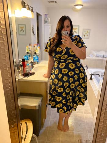 Reviewer is wearing a black wrap dress with sunflowers throughout