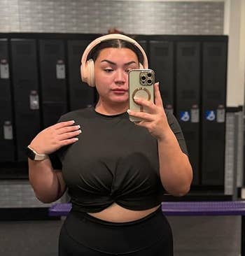 Person successful a gym locker country takes a reflector selfie wearing headphones and a knotted achromatic top
