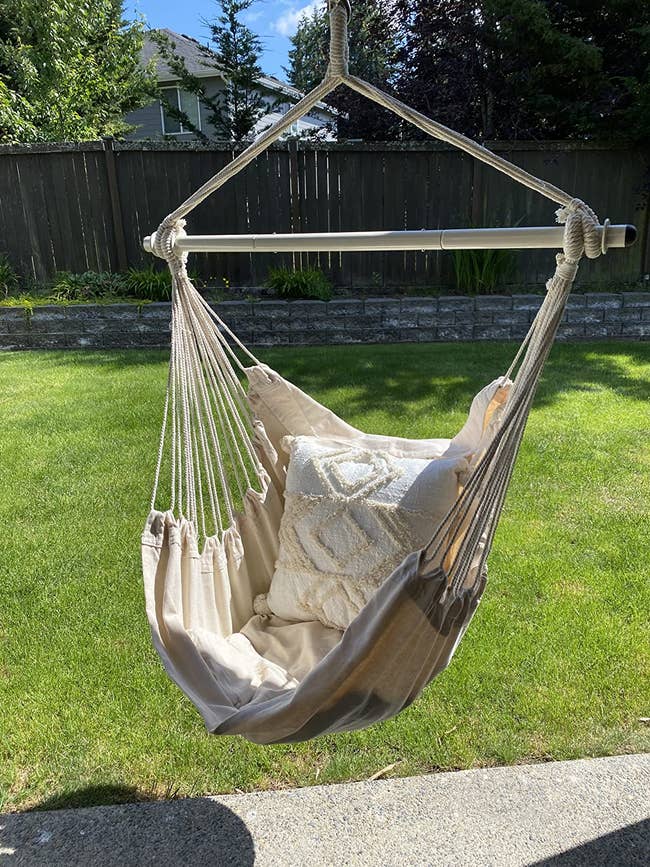 Hanging hammock chair with a white decorative pillow on a backyard lawn