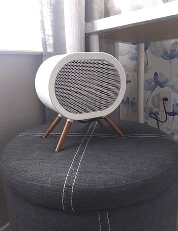 small white space heater sitting on gray ottoman