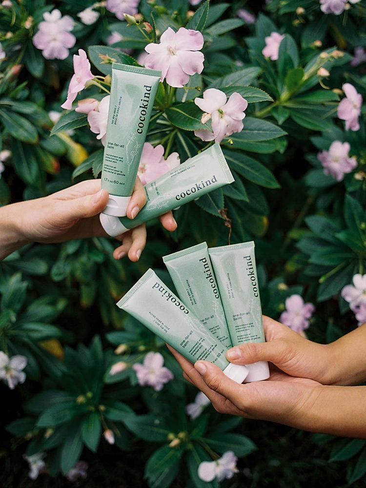 two pairs of hands holding green tubes of the balm