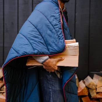 model wearing the navy blanket around their shoulders while holding firewood 
