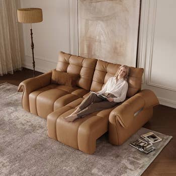 Woman relaxing connected  a reclining brownish  leather sectional sofa, speechmaking  a book. Room features a level  lamp and a modern  rug