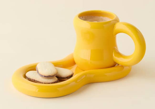 Unique ceramic mug with a wavy attached saucer holding 3 tiny cookies, perfect for stylish drinkware shopping