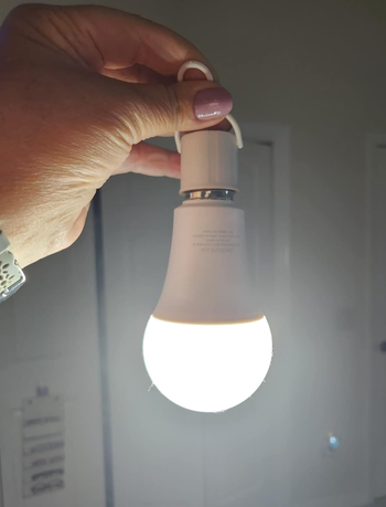Reviewer holding lit portable lightbulb upside down 