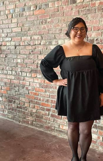reviewer wearing the black dress with tights and flats