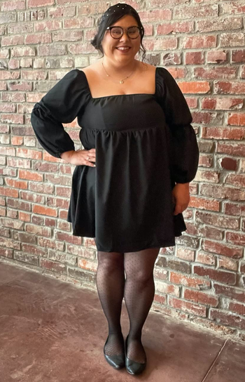 reviewer wearing the black dress with tights and flats