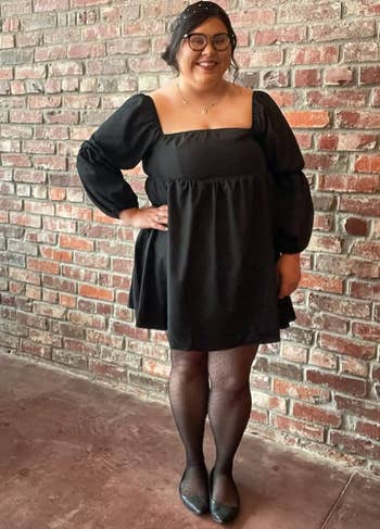 reviewer wearing the black dress with tights and flats